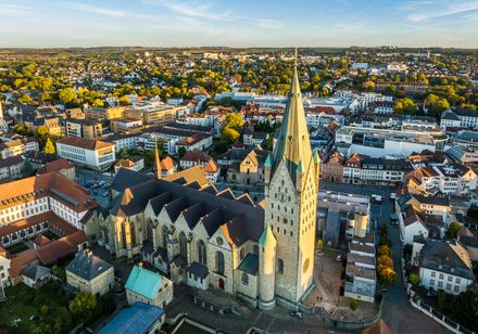 Luftaufnahme einer historischen Kirche mit spitzem Turm inmitten einer Stadtlandschaft bei Sonnenuntergang.