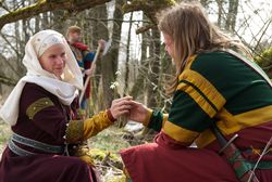 Mittelalterlich gekleidete Personen tauschen Schneeglöckchen aus, während ein weiterer im Hintergrund steht.