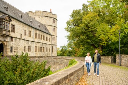 Ein Paar spaziert lächelnd auf einem gepflasterten Weg entlang der historischen Wewelsburg in Büren.