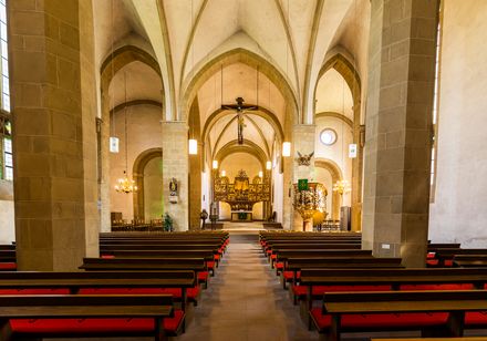 Kircheninnenraum mit hohen Gewölbedecken, hölzernen Bänken und einem kunstvollen Altar im Hintergrund.