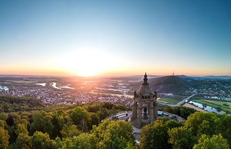 Panoramablick auf das Kaiser-Wilhelm-Denkmal bei Sonnenuntergang, umgeben von üppiger Landschaft.