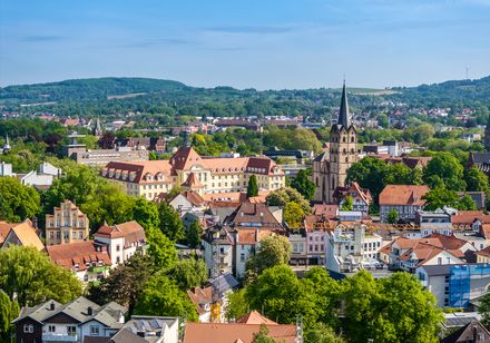 Stadtansicht von Herford mit grünen Bäumen, markanten Kirchen und Gebäuden im Hintergrund.