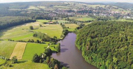 Luftaufnahme des Nethestausees, umgeben von dichten Wäldern und Feldern, Dorf im Hintergrund.