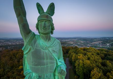 Arminius-Statue im Abendlicht, umgeben von Wäldern mit weitem Blick über die Landschaft.
