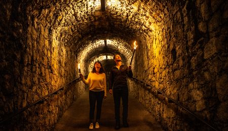Zwei Personen mit Fackeln erkunden einen historischen unterirdischen, steinernen Tunnel in Bielefeld.