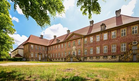 Klosteranlage Clarholz mit barockem Backsteingebäude, umgeben von Bäumen und grüner Wiese.