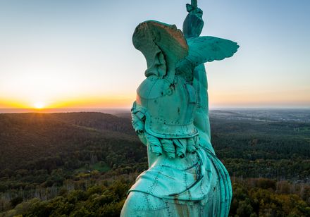 Hermannsdenkmal bei Sonnenuntergang, zeigt den Rücken der Statue mit ausgebreiteten Flügeln zur Landschaft.