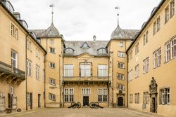 <p>Historisches Schloss mit gelber Fassade, Zinnen und Kanonen im Innenhof, unter bewölktem Himmel.</p>