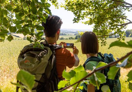Ein Paar mit Rucksäcken genießt den weiten Blick über ein grünes Feld bei Marienmünster.