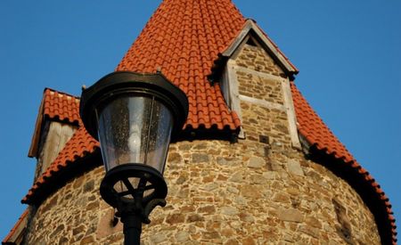 Runder mittelalterlicher Turm aus Stein mit rotem Ziegeldach, beleuchtet von einer Straßenlampe.