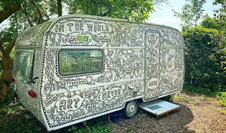 Erbsen im Grünen verweilt ein künstlerisch bemalter, detailreich verzierter Wohnwagen.