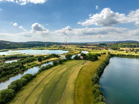 Luftaufnahme einer idyllischen Flusslandschaft mit Feldern, Seen und Hügeln unter blauem Himmel.