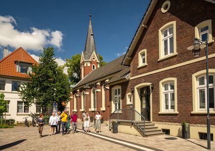 Eine Gruppe von Menschen steht vor einem historischen Backsteingebäude mit Spitzdach.